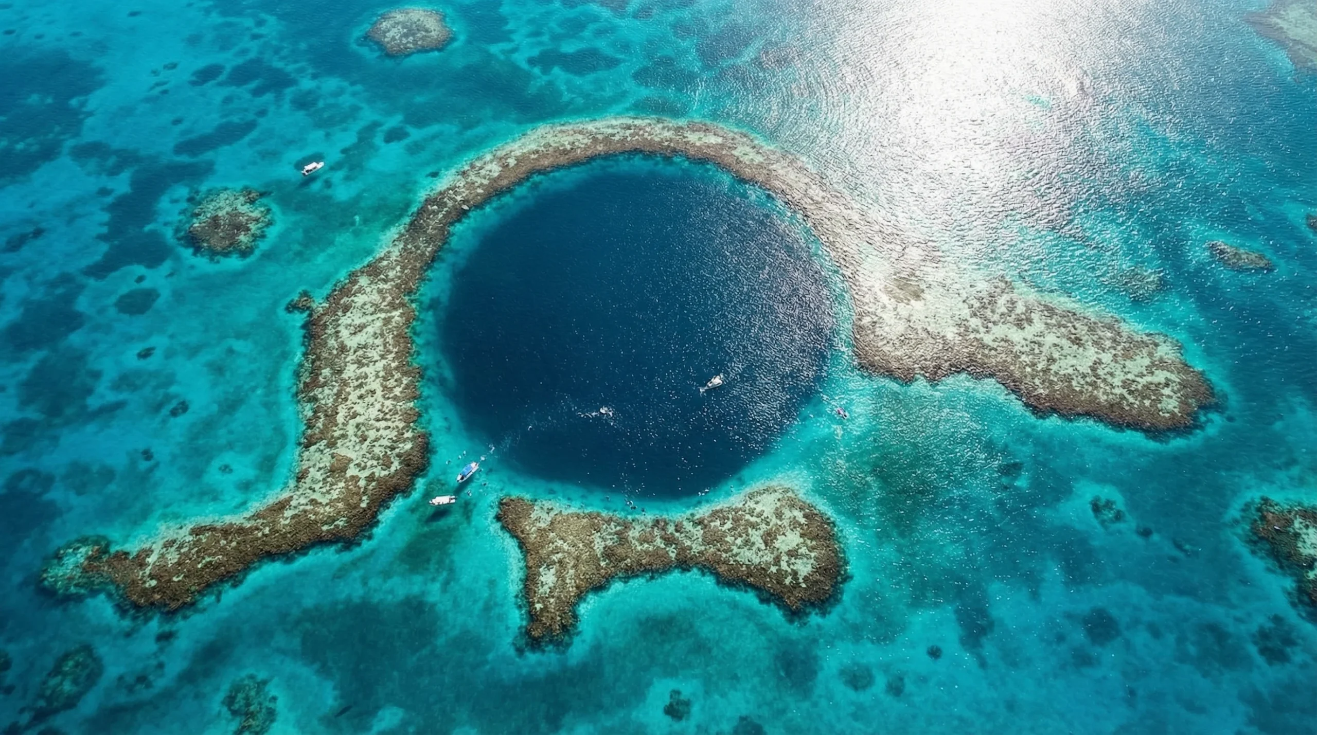 Aerial view of the Great Blue Hole in Belize, showcasing its circular shape surrounded by vibrant coral reefs and turquoise waters, with boats nearby for exploration.